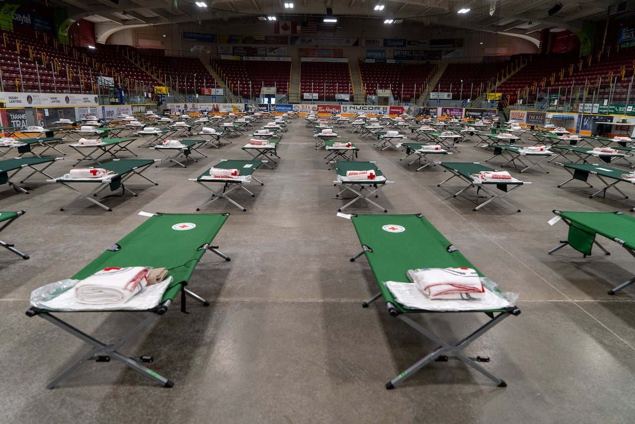 default-688 Dozens of green cots are set up on the concrete floor of an arena.