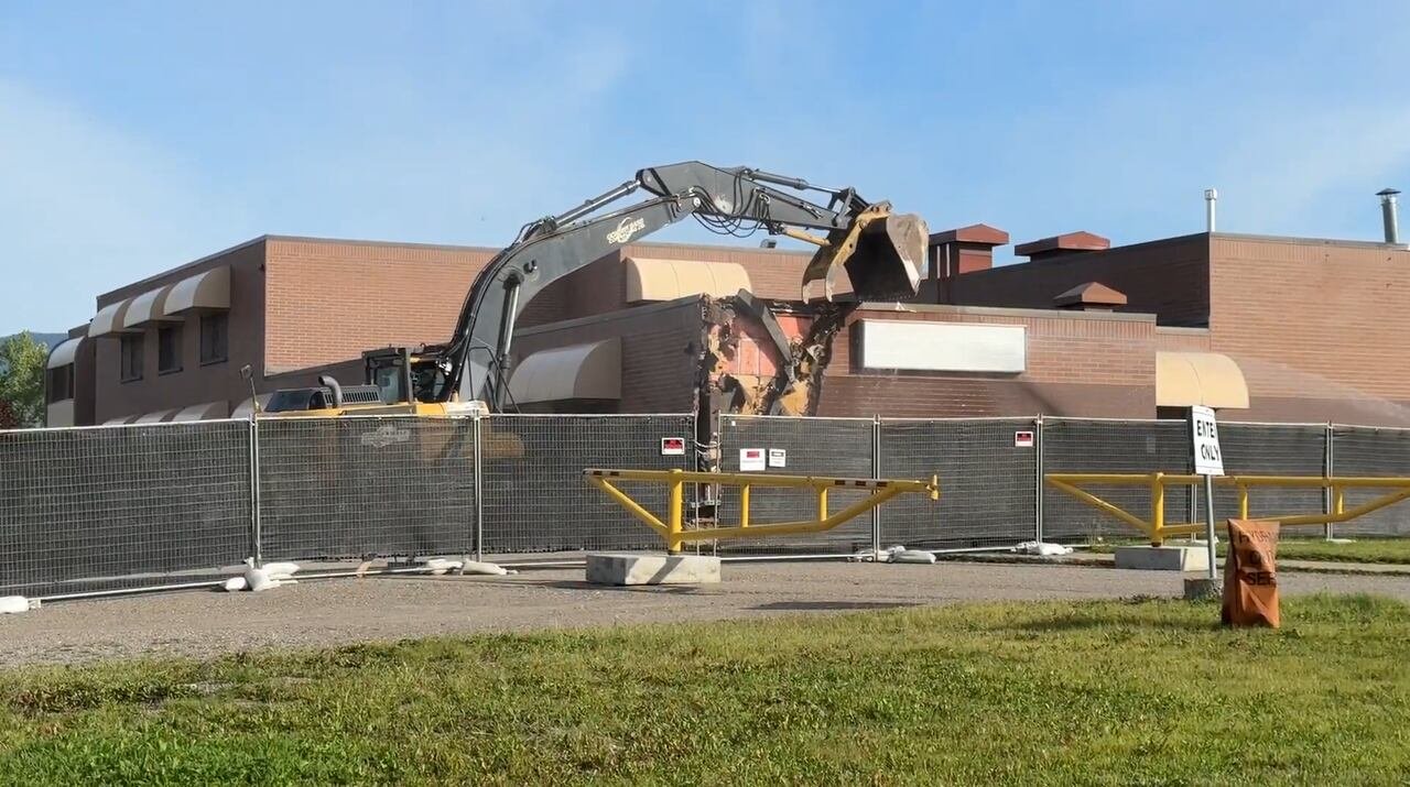 An excavator is pictured tearing down the corner of a building, exposing bricks on its corner.