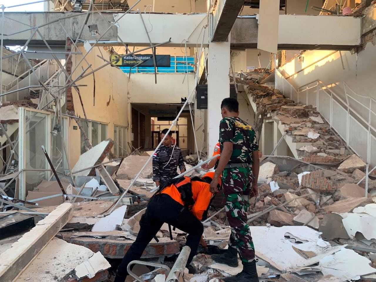 Men in uniforms search through rubble and debris in a destroyed building.