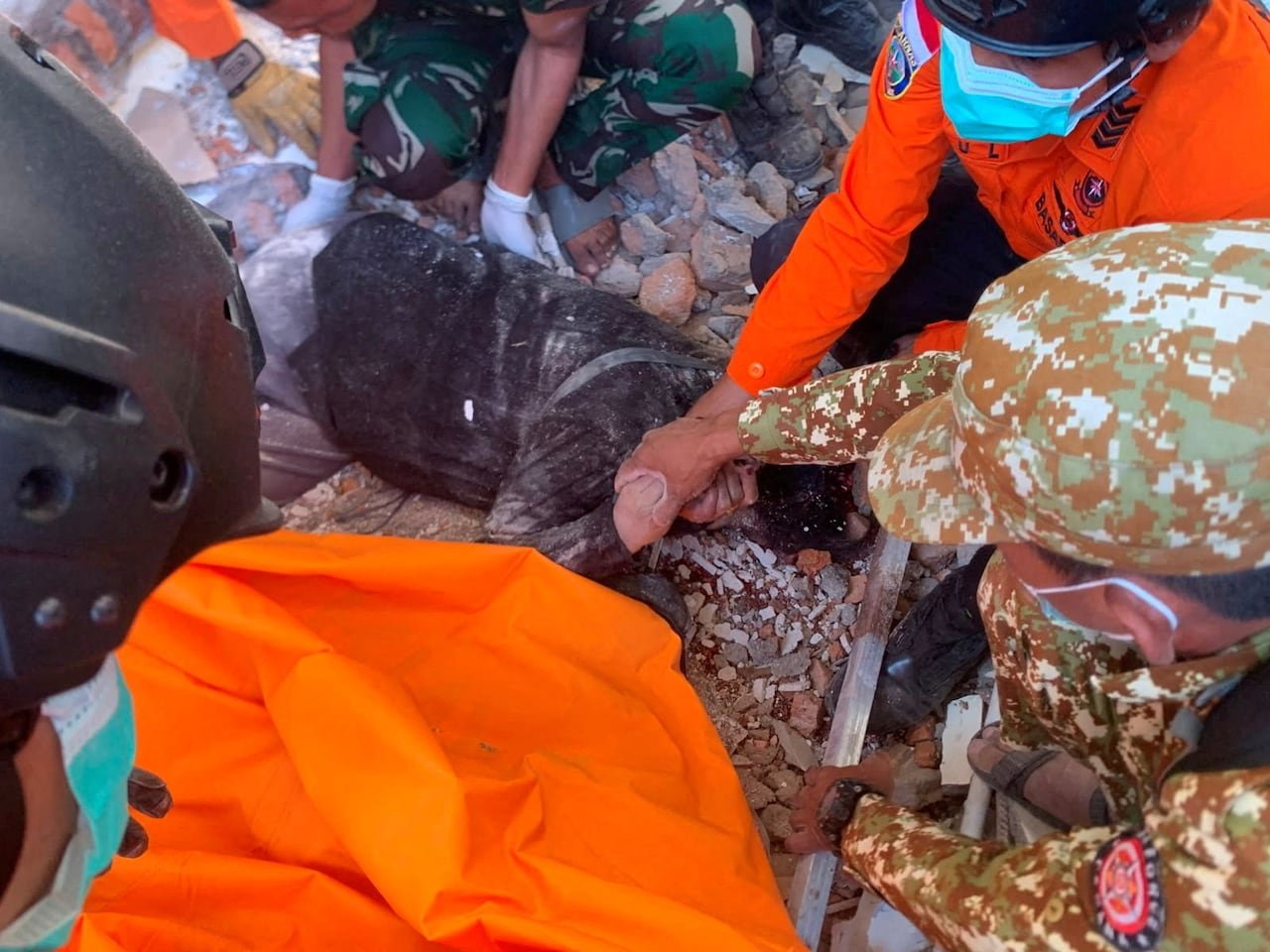 A team of rescuers pull a person out of rubble.